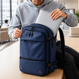 A navy blue laptop backpack with straps and zippers, shown on a table with a person in a hoodie holding a silver laptop inside it.