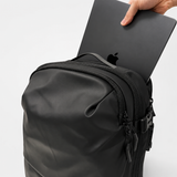 A black backpack shown close-up with a hand inserting a laptop into its top pocket. The Apple logo is visible on the laptop, but since the laptop is a prop and not the product being sold, no brand is listed under visible_brands.