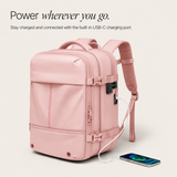 A light pink backpack with multiple zippered compartments, padded shoulder straps, and a built-in USB-C charging port, shown with a smartphone connected via a white cable on a light beige background. Text at the top reads, 'Power wherever you go.