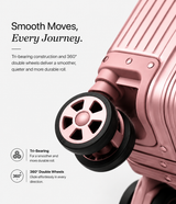 Close-up of a pink hard-shell suitcase wheel with trim and text callouts describing smooth tri-bearing construction and 360° double wheels on a light gray background.