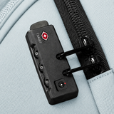 A close-up of a TSA combination lock with a red logo, mounted on a light blue fabric bag next to a zipper.